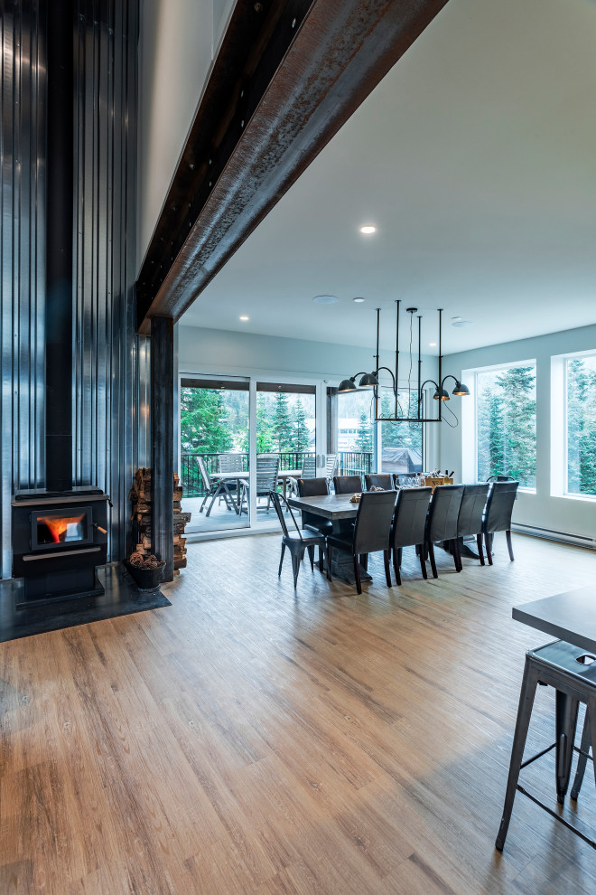 Design ideas for an expansive modern kitchen/dining combo in Vancouver with white walls, vinyl floors, a wood stove, a metal fireplace surround and brown floor.