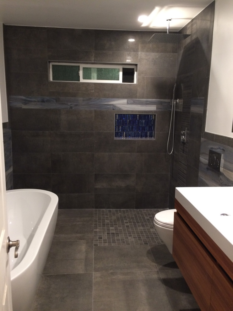 Inspiration for a mid-sized modern master bathroom in Orange County with flat-panel cabinets, medium wood cabinets, a freestanding tub, a curbless shower, a wall-mount toilet, blue tile, ceramic tile, white walls, ceramic floors, an integrated sink, engineered quartz benchtops, grey floor, an open shower, white benchtops, a niche, a double vanity, a floating vanity and decorative wall panelling.