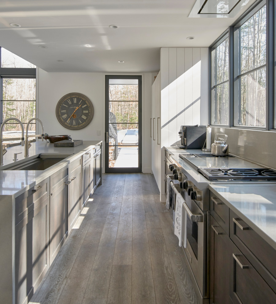 Design ideas for a mid-sized country open plan kitchen in Chicago with an undermount sink, shaker cabinets, grey cabinets, quartz benchtops, grey splashback, engineered quartz splashback, panelled appliances, light hardwood floors, with island, grey floor and grey benchtop.