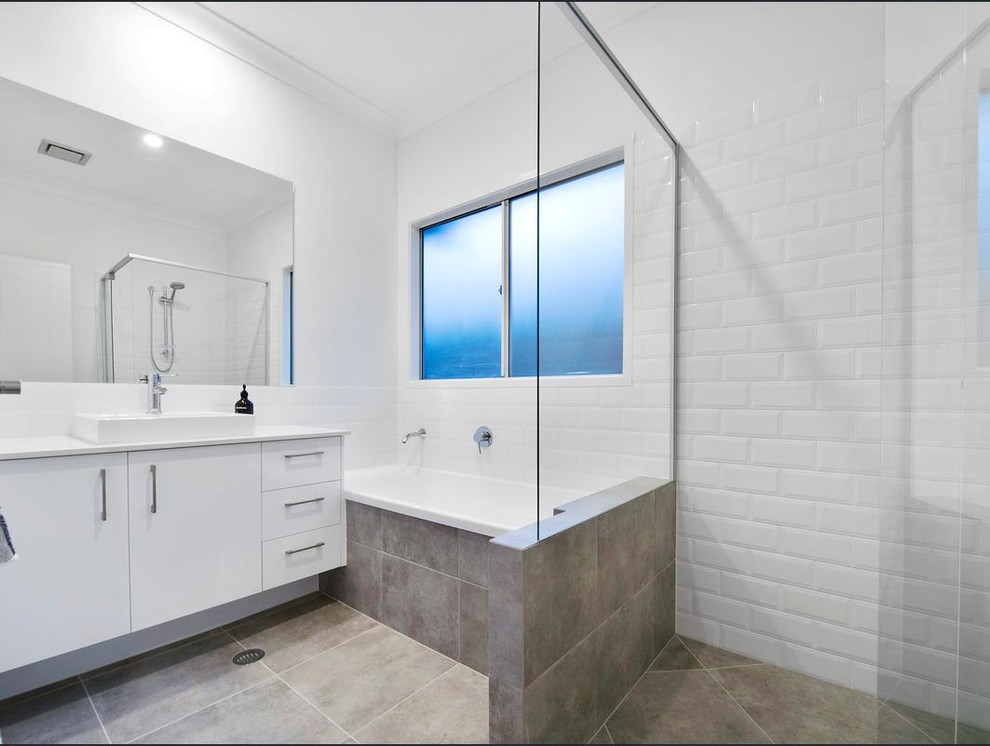 This is an example of a mid-sized contemporary master bathroom in Brisbane with flat-panel cabinets, white cabinets, a drop-in tub, white tile, ceramic tile, white walls, ceramic floors, a vessel sink, engineered quartz benchtops and a corner shower.