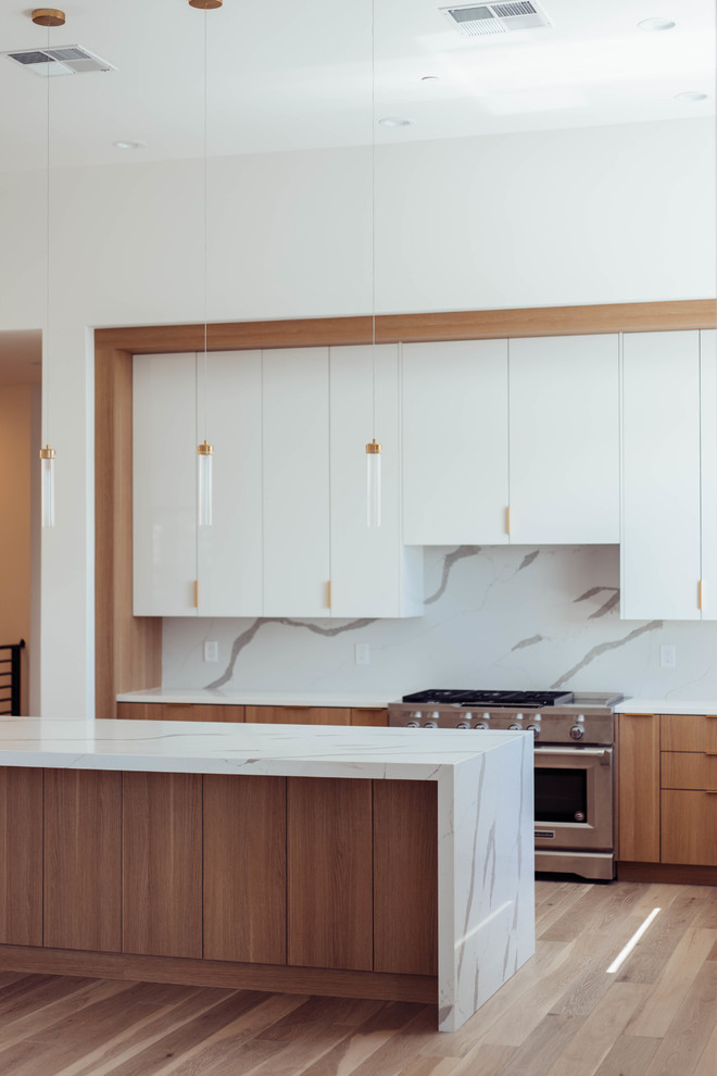 This is an example of a mid-sized contemporary l-shaped open plan kitchen in Sacramento with an undermount sink, flat-panel cabinets, white cabinets, quartz benchtops, white splashback, stone slab splashback, stainless steel appliances, medium hardwood floors, with island, brown floor and white benchtop.