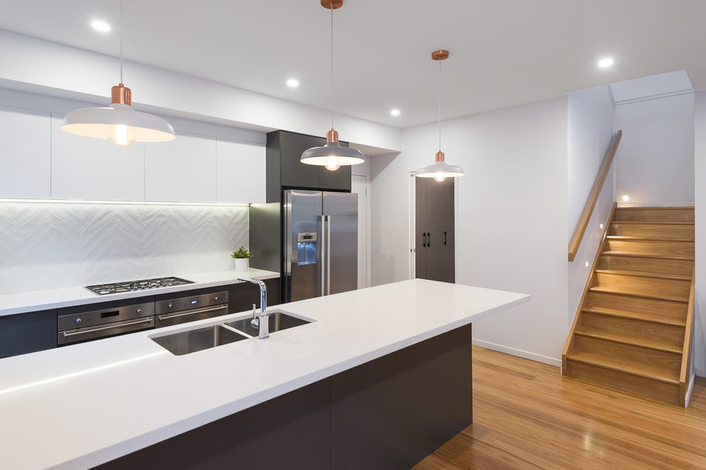 Photo of a mid-sized contemporary galley eat-in kitchen in Brisbane with a double-bowl sink, flat-panel cabinets, grey cabinets, quartz benchtops, white splashback, ceramic splashback, stainless steel appliances, light hardwood floors and with island.