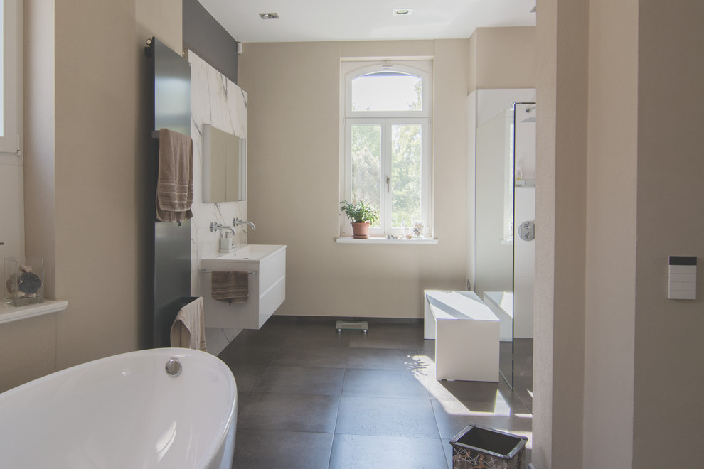 Badezimmer With flächenbündigen Schrankfronten, weißen Schränken, freistehender Badewanne, Wandtoilette, schwarzen Fliesen, Porzellanfliesen, beiger Wandfarbe, Porzellan-Bodenfliesen, integriertem Waschbecken and Mineralwerkstoff-Waschtisch in Leipzig