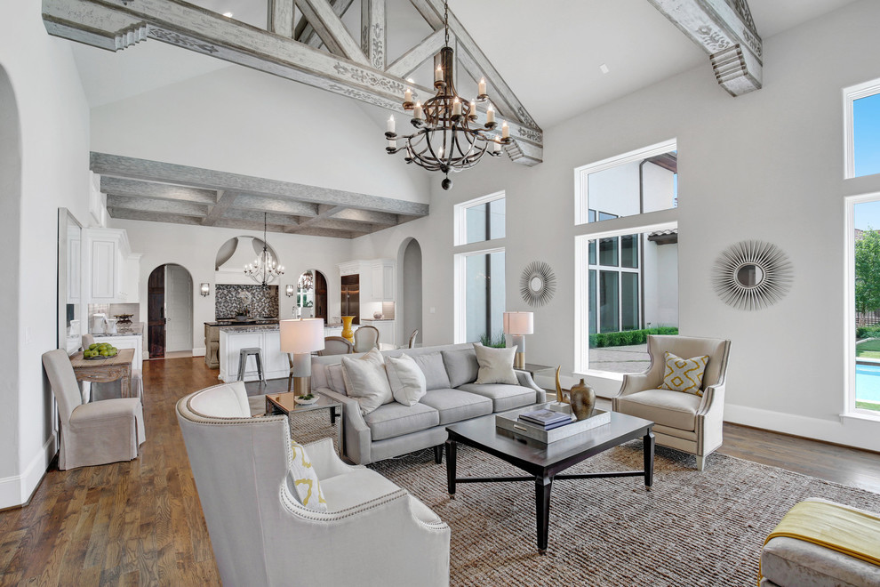 Design ideas for a large mediterranean open concept family room in Dallas with a home bar, grey walls, medium hardwood floors, a standard fireplace, a stone fireplace surround and brown floor.