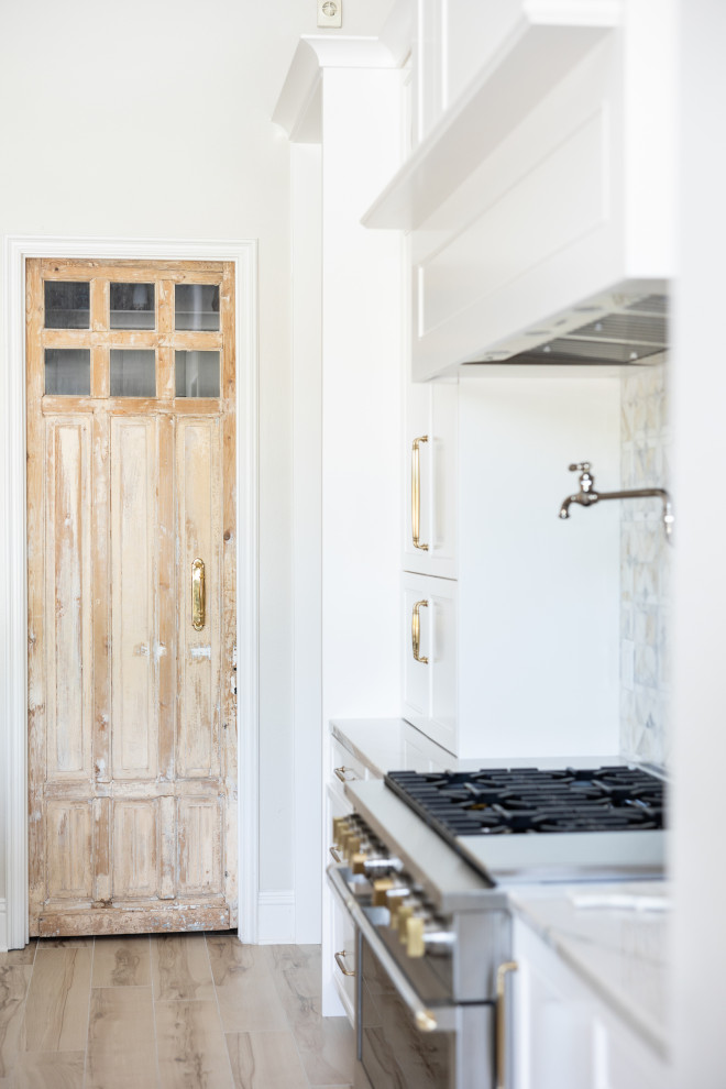 Inspiration for a large transitional porcelain tile and beige floor kitchen remodel in Orlando with a farmhouse sink, recessed-panel cabinets, white cabinets, quartzite countertops, multicolored backsplash, marble backsplash, stainless steel appliances, an island and beige countertops