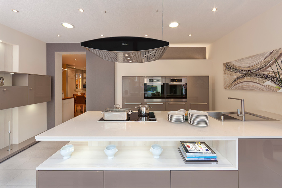 Mid-sized contemporary galley open plan kitchen in Dortmund with flat-panel cabinets, beige cabinets, with island, a drop-in sink, solid surface benchtops, stainless steel appliances and concrete floors.