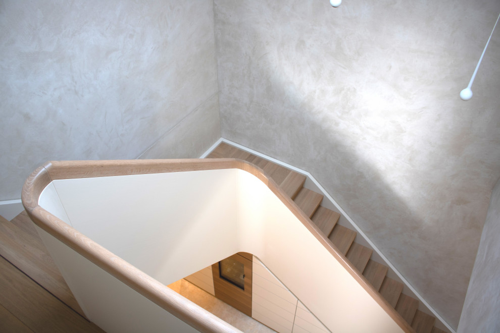 Expansive modern wood curved staircase in Other with wood risers, wood railing and wallpaper.