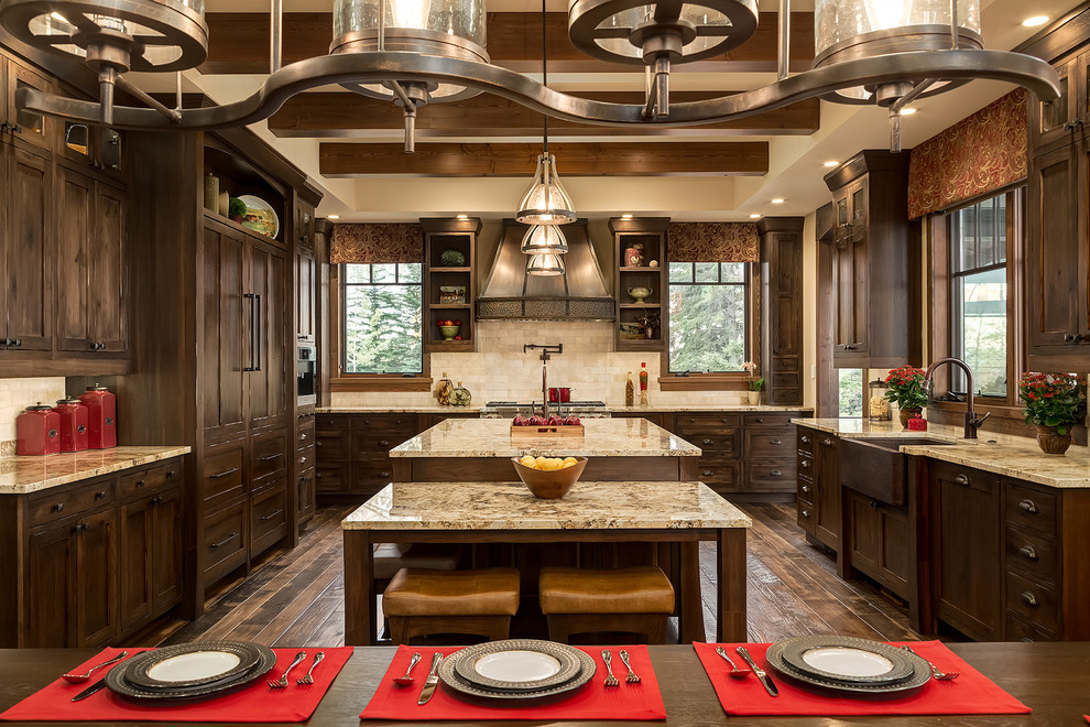 Design ideas for a large country u-shaped eat-in kitchen in Calgary with a farmhouse sink, shaker cabinets, dark wood cabinets, granite benchtops, beige splashback, panelled appliances, with island, dark hardwood floors and travertine splashback.