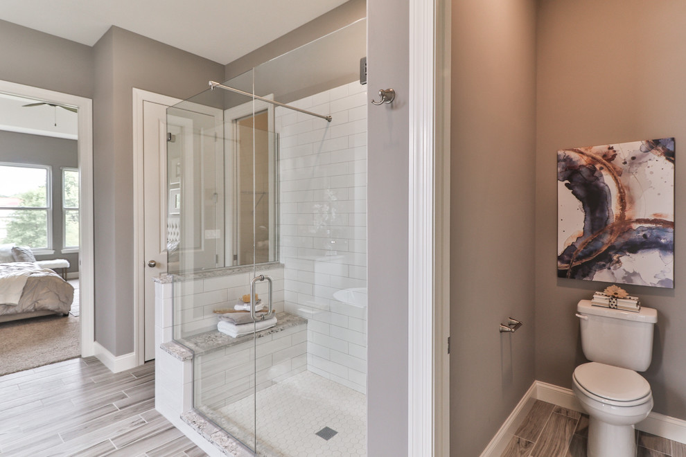 Inspiration for a mid-sized transitional master bathroom in St Louis with shaker cabinets, dark wood cabinets, a freestanding tub, an alcove shower, a two-piece toilet, white tile, porcelain tile, beige walls, vinyl floors, an undermount sink, granite benchtops, grey floor and a hinged shower door.
