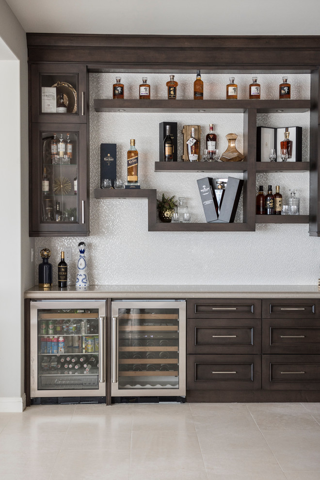 This is an example of a mid-sized contemporary l-shaped home bar in Orange County with an undermount sink, recessed-panel cabinets, dark wood cabinets, white splashback, limestone floors and white floor.