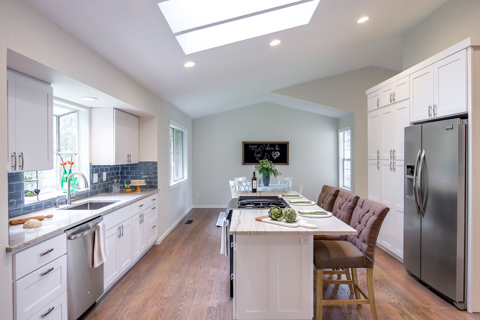 Inspiration for a large transitional galley medium tone wood floor and brown floor open concept kitchen remodel in Seattle with an undermount sink, shaker cabinets, white cabinets, quartz countertops, blue backsplash, subway tile backsplash, stainless steel appliances, an island and multicolored countertops