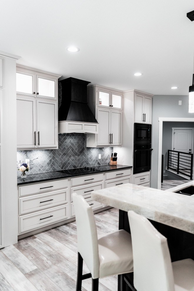 Huge transitional l-shaped laminate floor, gray floor and tray ceiling open concept kitchen photo with an undermount sink, flat-panel cabinets, white cabinets, quartz countertops, gray backsplash, ceramic backsplash, black appliances and an island