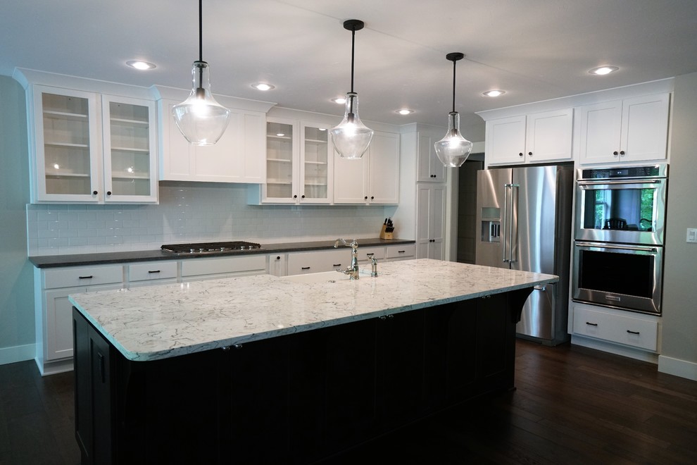Inspiration for a large transitional l-shaped dark wood floor and brown floor eat-in kitchen remodel with a farmhouse sink, shaker cabinets, white cabinets, marble countertops, white backsplash, subway tile backsplash, stainless steel appliances and an island