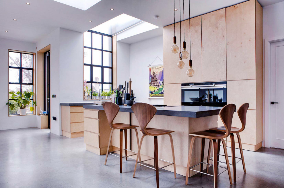 This is an example of a large scandinavian eat-in kitchen in Dublin with a drop-in sink, flat-panel cabinets, light wood cabinets, concrete benchtops, concrete floors, with island and black benchtop.