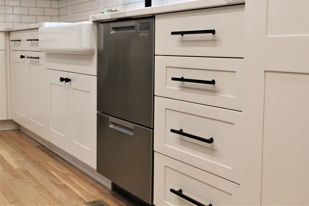 Eat-in kitchen - large transitional galley light wood floor eat-in kitchen idea with a farmhouse sink, shaker cabinets, white cabinets, quartz countertops, white backsplash, ceramic backsplash, stainless steel appliances, an island and white countertops