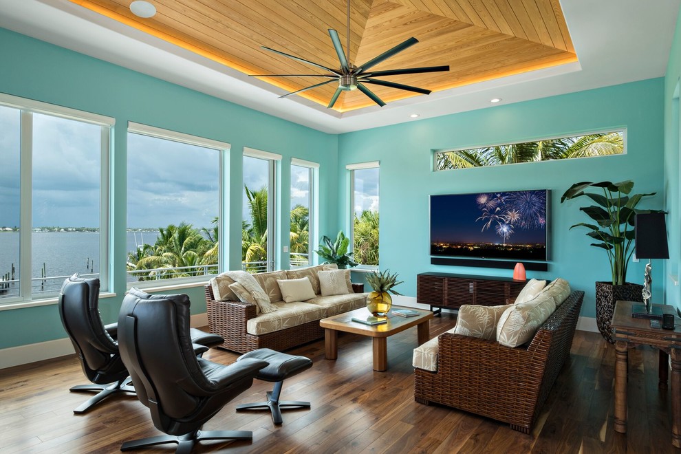 Design ideas for a tropical family room in Miami with blue walls, dark hardwood floors, no fireplace, a wall-mounted tv and brown floor.