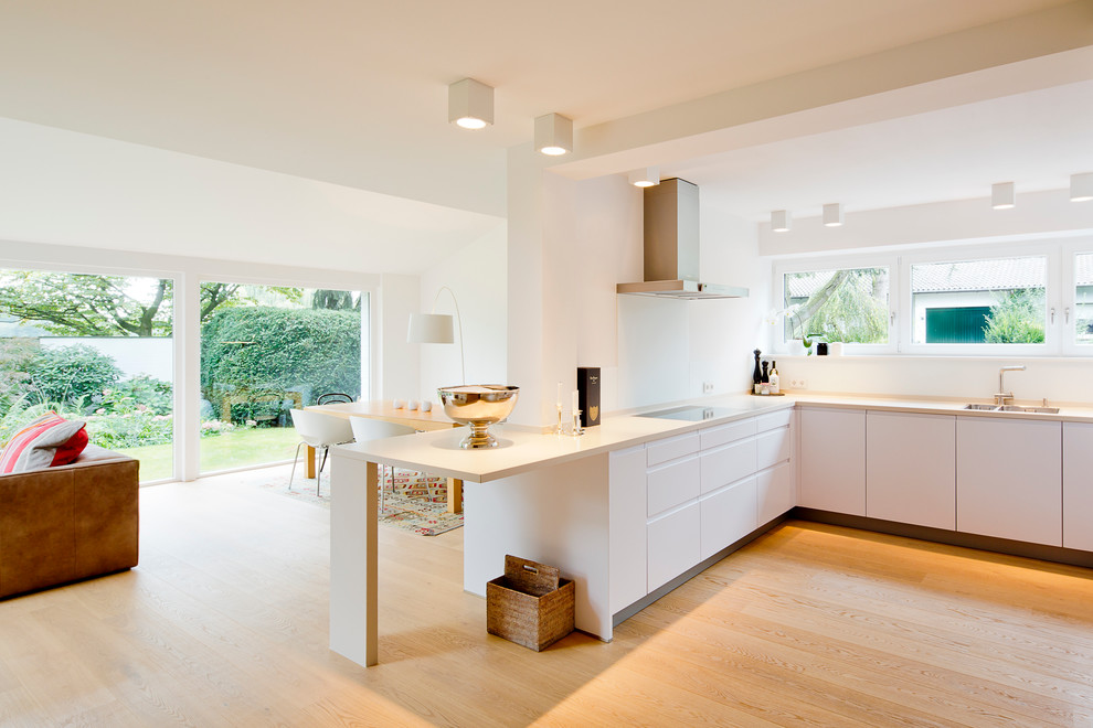 Design ideas for a large contemporary l-shaped open plan kitchen in Dusseldorf with an undermount sink, flat-panel cabinets, white cabinets, white splashback, panelled appliances and light hardwood floors.