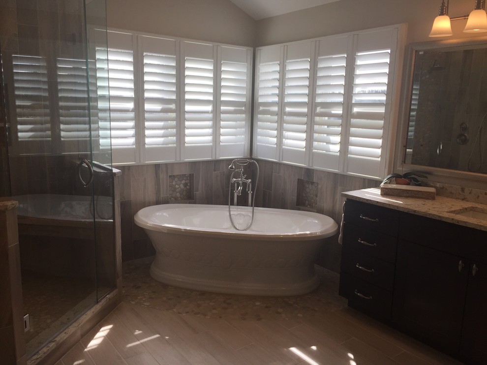 Inspiration for a large transitional master gray tile and porcelain tile light wood floor and brown floor freestanding bathtub remodel in Baltimore with shaker cabinets, dark wood cabinets, a two-piece toilet, beige walls, an undermount sink, solid surface countertops and a hinged shower door