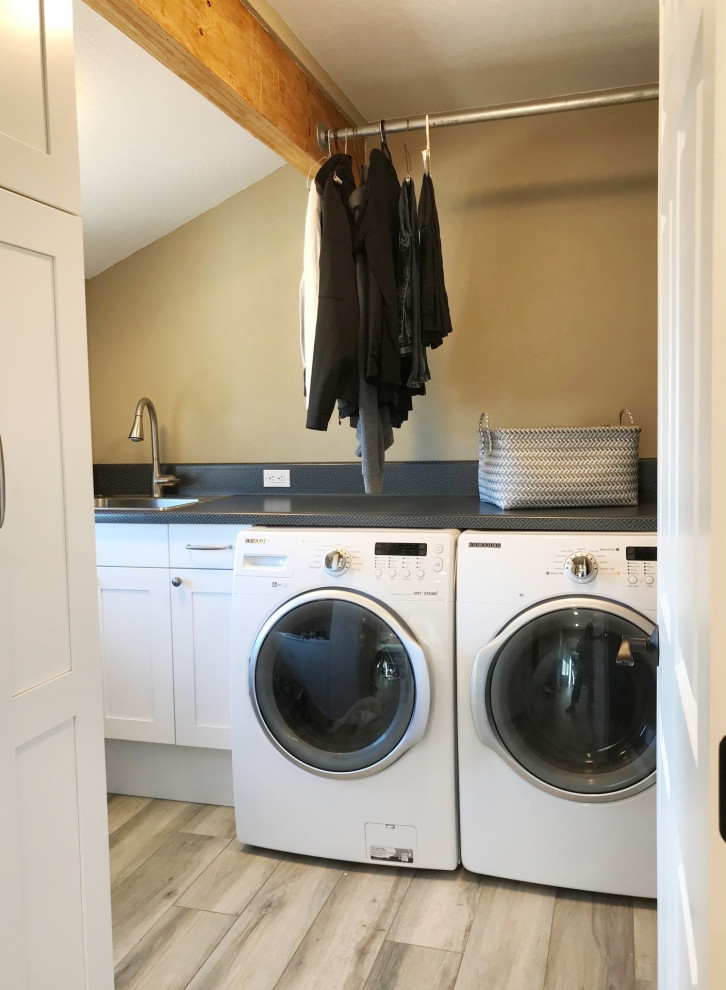 Photo of a small transitional u-shaped dedicated laundry room in San Diego with a drop-in sink, flat-panel cabinets, brown cabinets, laminate benchtops, black splashback, beige walls, porcelain floors, a side-by-side washer and dryer, grey floor, multi-coloured benchtop and exposed beam.
