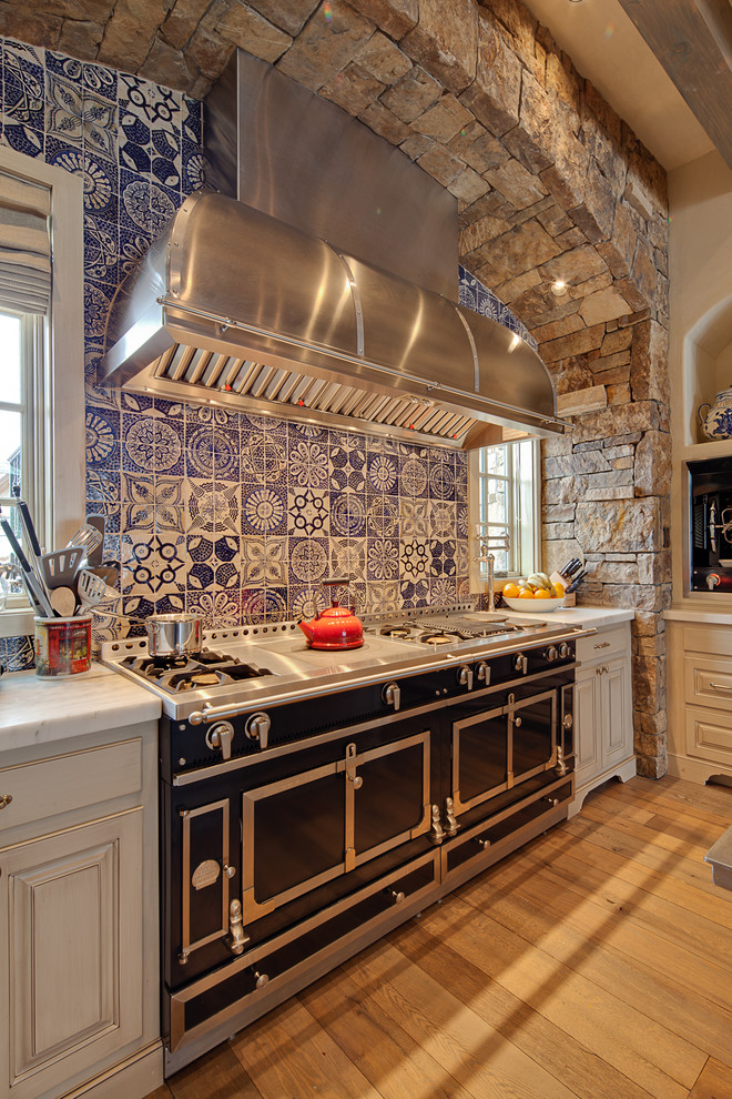 Photo of a country kitchen in Denver with raised-panel cabinets, blue splashback and black appliances.