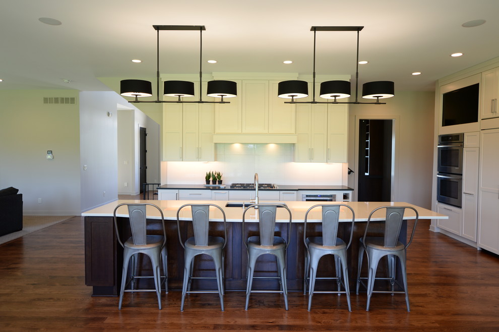 Large transitional single-wall medium tone wood floor open concept kitchen photo with an undermount sink, recessed-panel cabinets, white cabinets, granite countertops, white backsplash, stainless steel appliances and an island