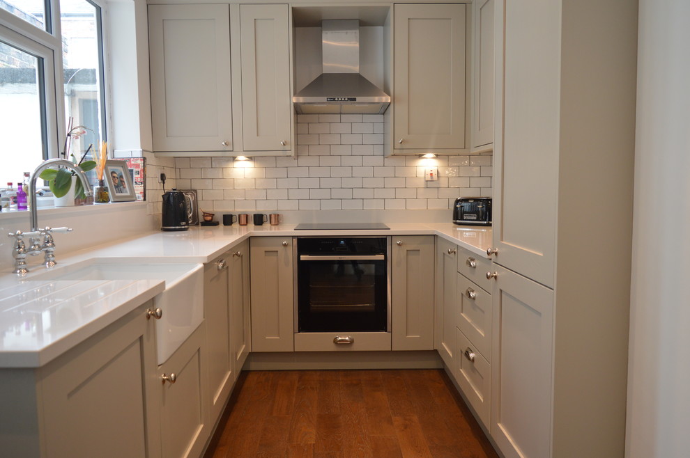 Small traditional u-shaped separate kitchen in Other with a farmhouse sink, shaker cabinets, grey cabinets, quartzite benchtops, white splashback, subway tile splashback, stainless steel appliances, dark hardwood floors, no island, brown floor and white benchtop.