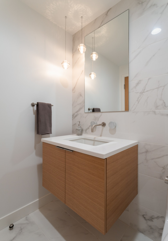 This is an example of a small modern powder room in Cincinnati with flat-panel cabinets, light wood cabinets, a one-piece toilet, white tile, ceramic tile, white walls, porcelain floors, an undermount sink, engineered quartz benchtops, white floor and white benchtops.
