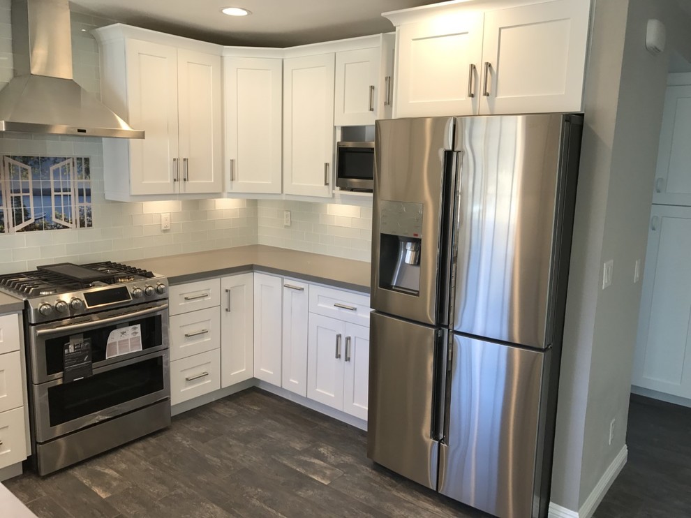 Mid-sized contemporary u-shaped eat-in kitchen in Los Angeles with a farmhouse sink, shaker cabinets, white cabinets, quartzite benchtops, glass tile splashback, stainless steel appliances, ceramic floors, no island, brown floor, grey benchtop and grey splashback.