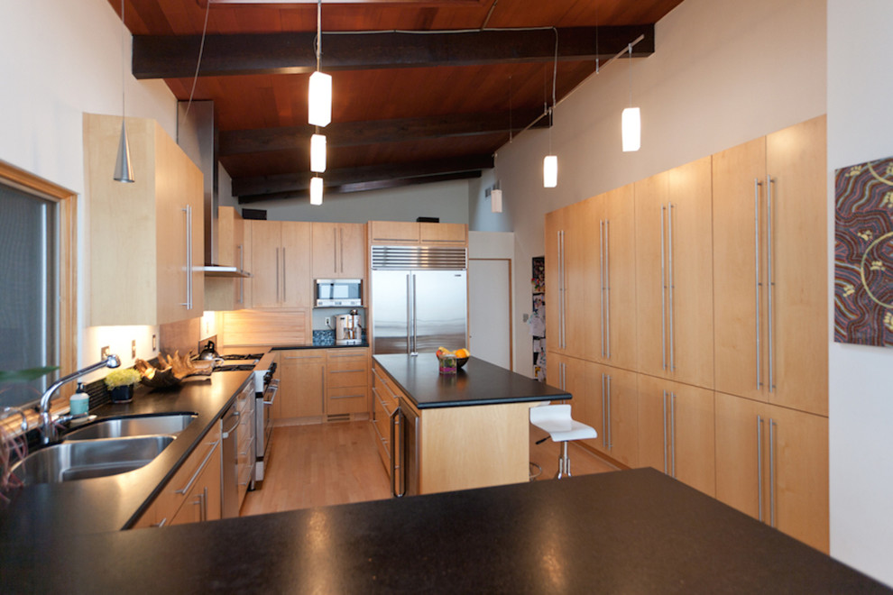 This is an example of a midcentury kitchen in Portland with an undermount sink, flat-panel cabinets, light wood cabinets, granite benchtops, stainless steel appliances and light hardwood floors.