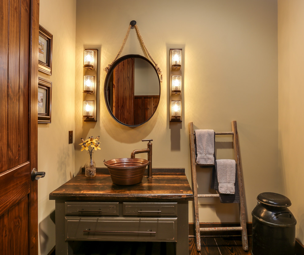 This is an example of a small country powder room in Raleigh with furniture-like cabinets, distressed cabinets, beige walls, a vessel sink, dark hardwood floors, wood benchtops, brown floor and brown benchtops.