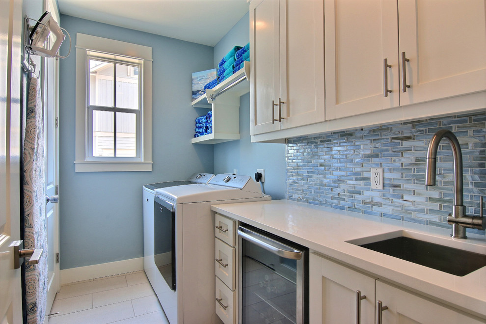 Mid-sized beach style galley utility room in Austin with an undermount sink, shaker cabinets, white cabinets, quartzite benchtops, blue walls, ceramic floors, a side-by-side washer and dryer and beige floor.