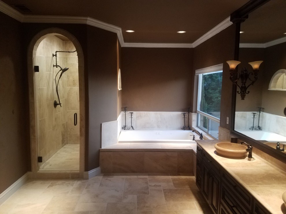 Large traditional master bathroom in Sacramento with raised-panel cabinets, dark wood cabinets, a drop-in tub, an alcove shower, beige tile, ceramic tile, brown walls, travertine floors, a vessel sink, beige floor, a hinged shower door and beige benchtops.