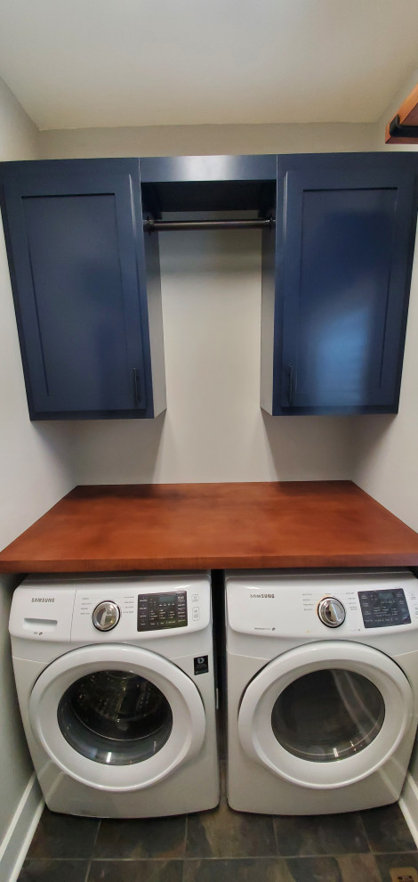 This is an example of a small contemporary galley utility room in Raleigh with shaker cabinets, blue cabinets, wood benchtops, grey walls, ceramic floors, a side-by-side washer and dryer, blue floor and red benchtop.