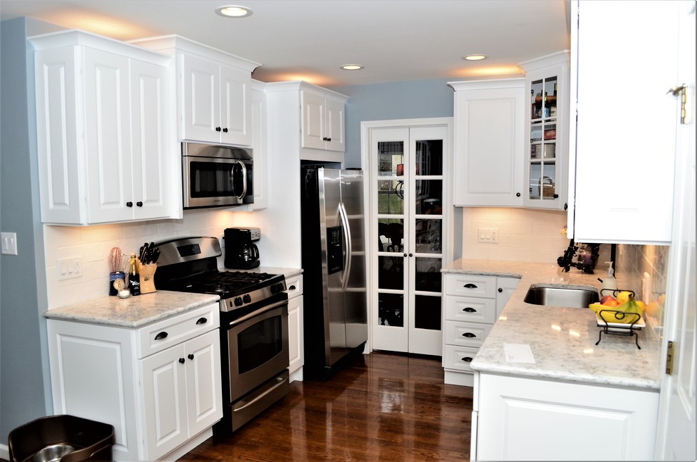 Photo of a mid-sized transitional l-shaped eat-in kitchen in Other with an undermount sink, raised-panel cabinets, white cabinets, quartzite benchtops, white splashback, subway tile splashback, stainless steel appliances, medium hardwood floors, no island, brown floor and white benchtop.