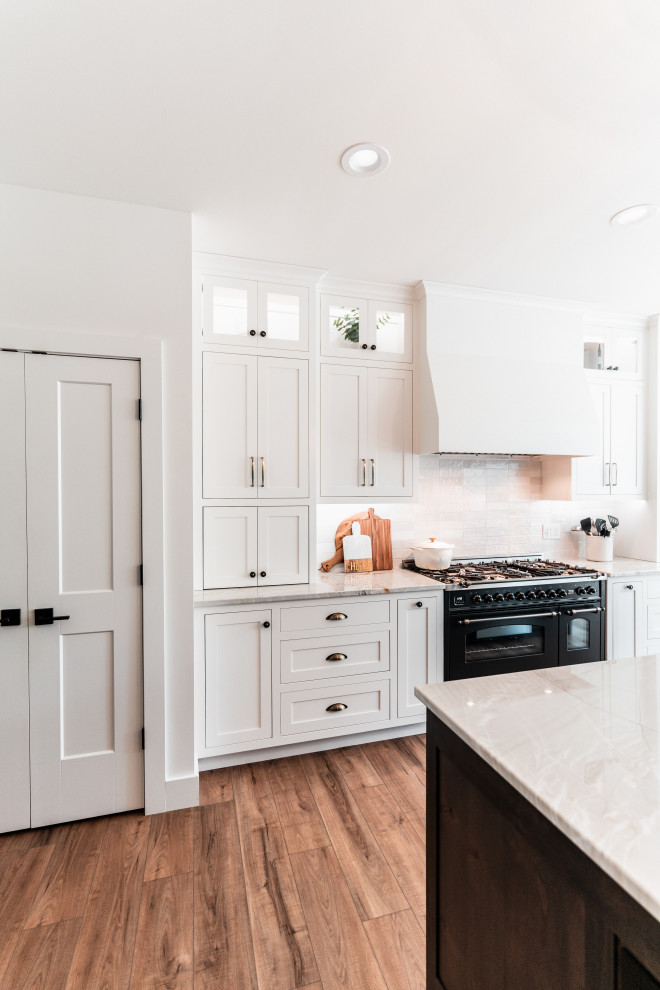 Open concept kitchen - large transitional l-shaped light wood floor open concept kitchen idea with an undermount sink, shaker cabinets, white cabinets, quartzite countertops, multicolored backsplash, porcelain backsplash, stainless steel appliances and an island