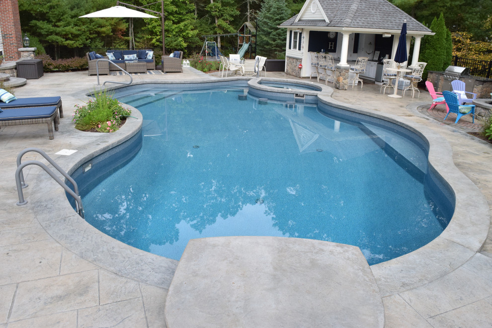 Photo of a mid-sized traditional backyard kidney-shaped lap pool in Providence with a pool house and stamped concrete.