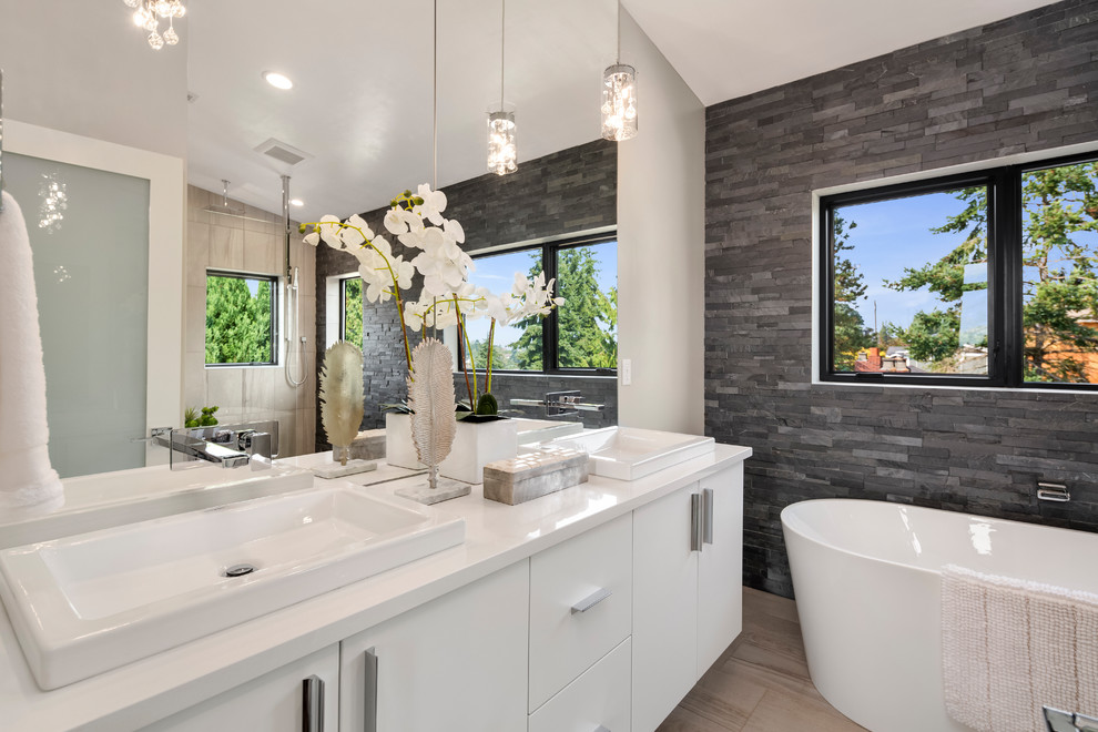 Design ideas for a mid-sized contemporary master bathroom in Los Angeles with flat-panel cabinets, white cabinets, a freestanding tub, an alcove shower, gray tile, stone tile, grey walls, porcelain floors, a drop-in sink, solid surface benchtops, beige floor, a hinged shower door and white benchtops.