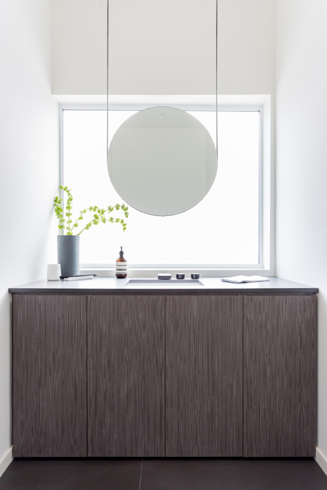Inspiration for a mid-sized modern powder room in Los Angeles with flat-panel cabinets, medium wood cabinets, a one-piece toilet, white walls, porcelain floors, an undermount sink, engineered quartz benchtops, grey floor, grey benchtops, a built-in vanity and vaulted.