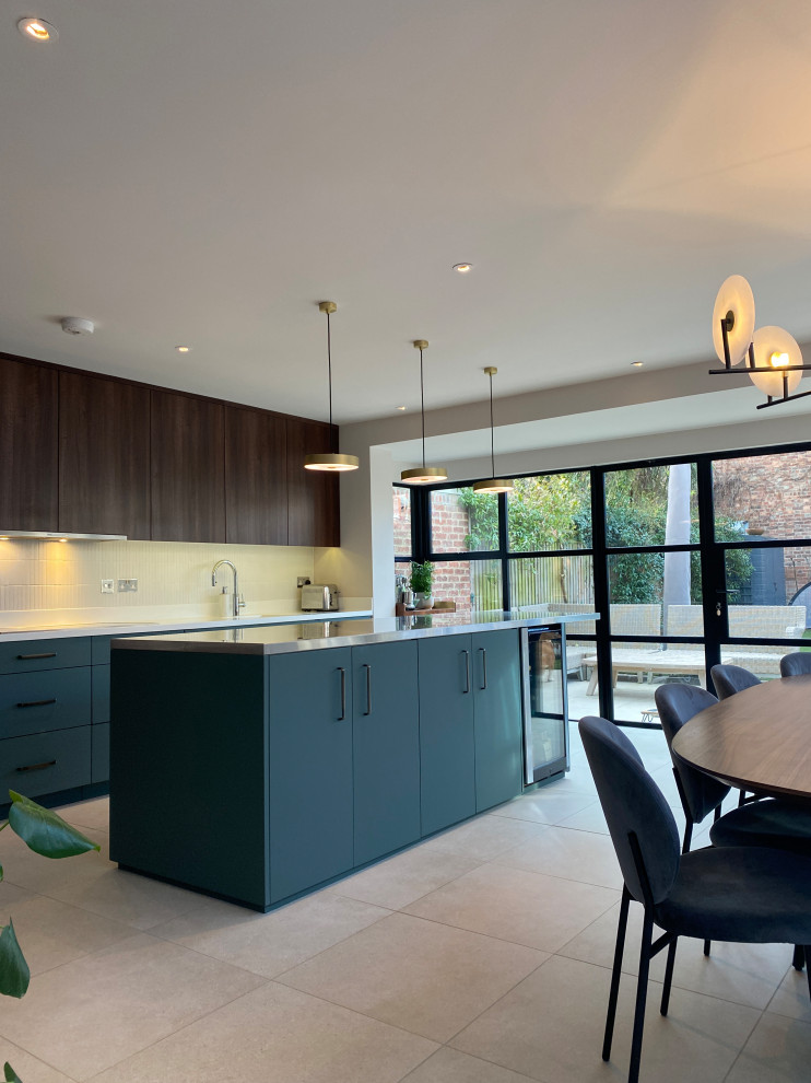 This is an example of a large contemporary single-wall eat-in kitchen in London with a drop-in sink, flat-panel cabinets, dark wood cabinets, stainless steel benchtops, white splashback, ceramic splashback, stainless steel appliances, porcelain floors, with island, grey floor and grey benchtop.