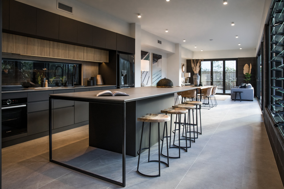 Inspiration for a large industrial galley open plan kitchen in Brisbane with recessed-panel cabinets, black cabinets, laminate benchtops, grey splashback, engineered quartz splashback, black appliances, ceramic floors, with island, grey floor and brown benchtop.