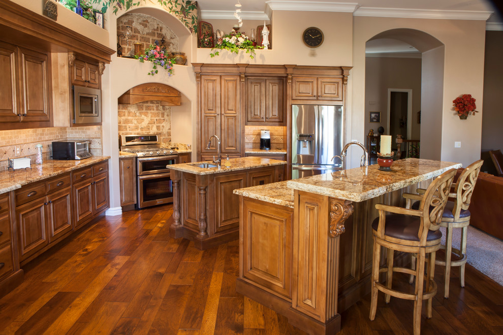 This is an example of a mid-sized traditional l-shaped eat-in kitchen in Phoenix with raised-panel cabinets, medium wood cabinets, granite benchtops, beige splashback, stone tile splashback, stainless steel appliances, medium hardwood floors and an undermount sink.