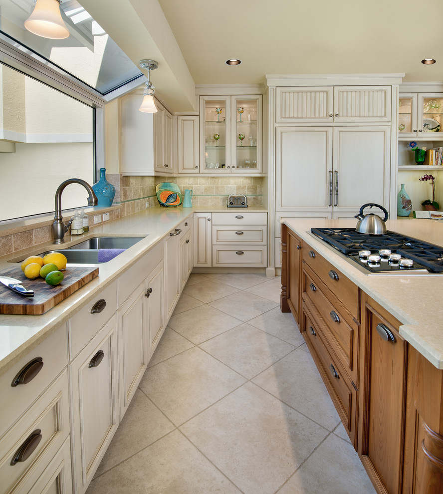 This is an example of a mid-sized beach style l-shaped eat-in kitchen in Miami with an undermount sink, recessed-panel cabinets, light wood cabinets, limestone benchtops, beige splashback, stone tile splashback, panelled appliances, porcelain floors and with island.