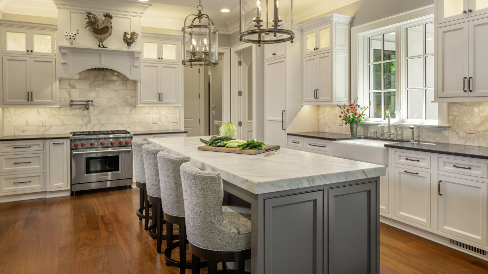 Large traditional l-shaped kitchen in Charlotte with a farmhouse sink, beaded inset cabinets, white cabinets, quartz benchtops, white splashback, marble splashback, stainless steel appliances, dark hardwood floors, with island, brown floor and black benchtop.