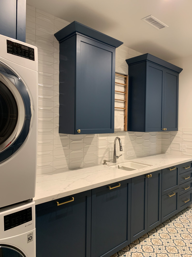 オレンジカウンティにある高級な中くらいなビーチスタイルのおしゃれな洗濯室 (ll型、ダブルシンク、シェーカースタイル扉のキャビネット、青いキャビネット、クオーツストーンカウンター、白いキッチンパネル、セラミックタイルのキッチンパネル、白い壁、セラミックタイルの床、上下配置の洗濯機・乾燥機、マルチカラーの床、白いキッチンカウンター) の写真