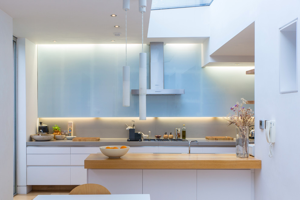 This is an example of a contemporary galley eat-in kitchen in London with flat-panel cabinets, white cabinets, wood benchtops, grey splashback and a peninsula.