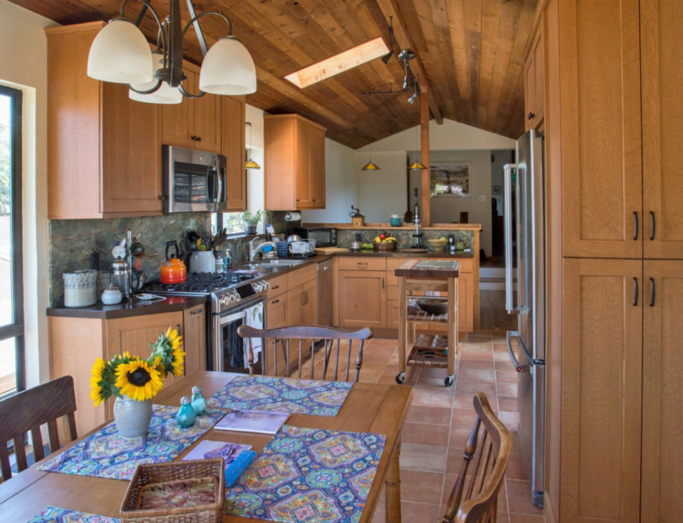 This is an example of a small country galley eat-in kitchen in San Luis Obispo with a double-bowl sink, recessed-panel cabinets, medium wood cabinets, quartz benchtops, green splashback, stone slab splashback, stainless steel appliances, terra-cotta floors, multi-coloured floor, brown benchtop and timber.
