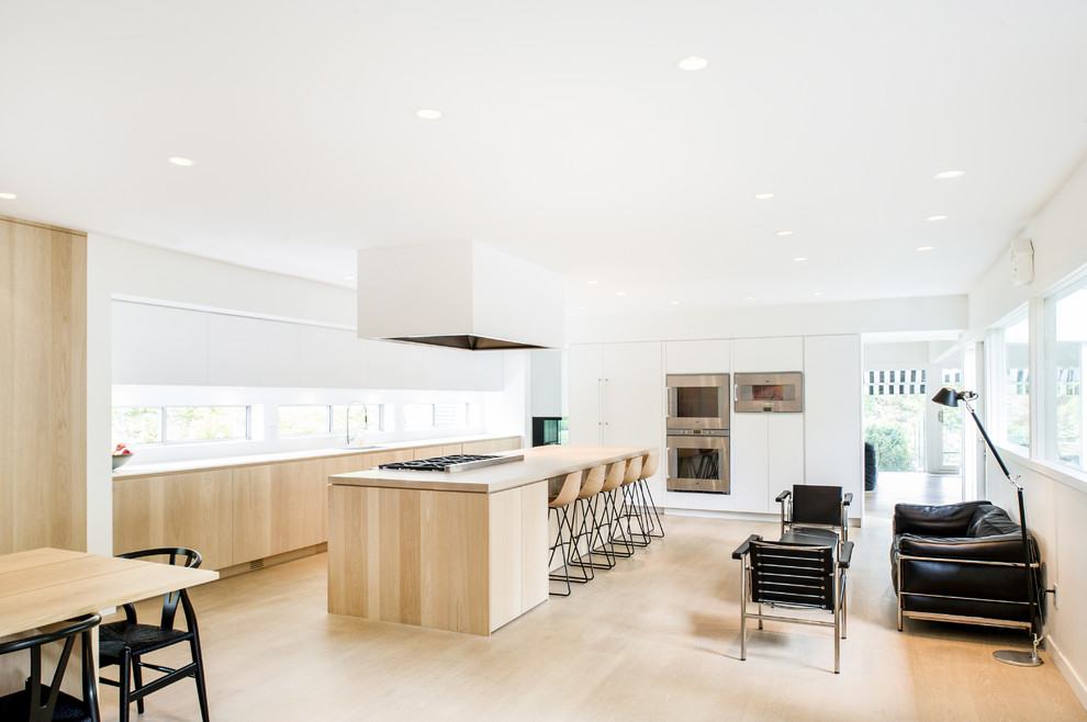Inspiration for a large midcentury open plan kitchen in Vancouver with an undermount sink, flat-panel cabinets, white cabinets, wood benchtops, white splashback, stainless steel appliances, light hardwood floors and with island.