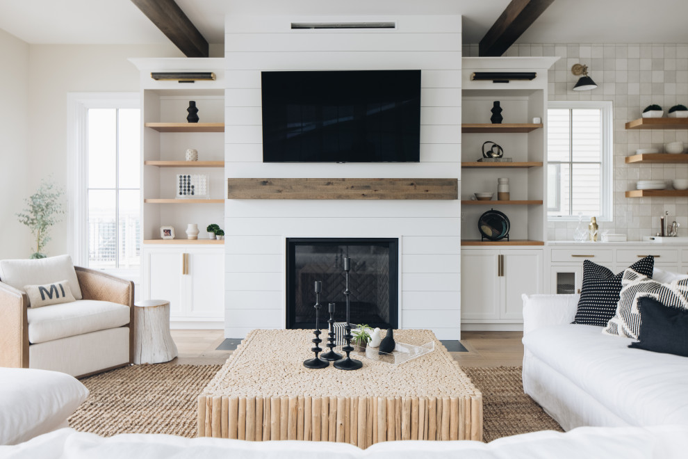 Design ideas for a beach style living room in Grand Rapids with white walls, light hardwood floors, a standard fireplace, a wall-mounted tv and exposed beam.