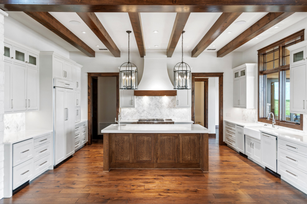 This is an example of a large country galley eat-in kitchen in Dallas with a farmhouse sink, shaker cabinets, white cabinets, quartzite benchtops, white splashback, porcelain splashback, panelled appliances, medium hardwood floors, with island, brown floor, white benchtop and exposed beam.