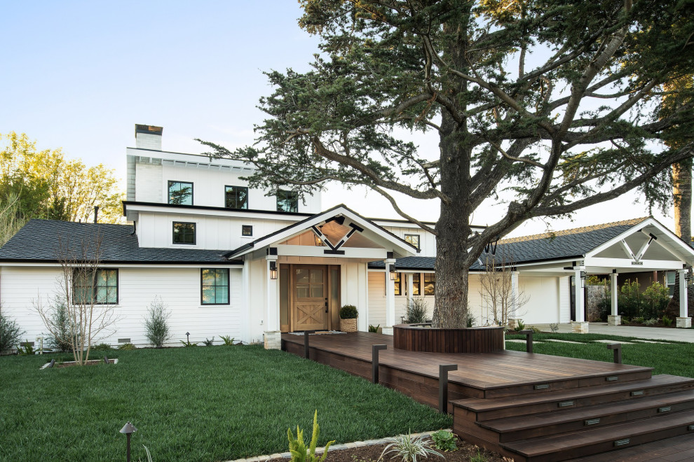 Esempio della villa grande bianca country a due piani con rivestimento con lastre in cemento, tetto a padiglione, copertura a scandole, tetto nero e pannelli e listelle di legno
